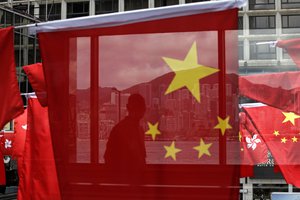 A man is reflected on a window as China and Kong Hong national flags are displayed outside a shopping center in Hong Kong Wednesday, June 28, 2017 to mark the 20th anniversary of Hong Kong handover to China. Hong Kong is planning a big party as it marks 20 years under Chinese rule. But many people in the former British colony are not in the mood to celebrate. (AP Photo/Kin Cheung)