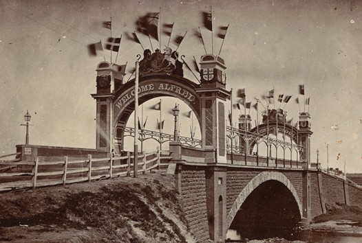 Sepia photograph of stone Princes Bridge crossing the Yarra River in Melbourne decorated with flags and bunting for the 1867 visit of Alfred, Duke of Edinburgh