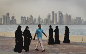 In this Saturday, April 7, 2012 file photo, with the new high-rise buildings of downtown Doha in the background, Qatari women and a man enjoy walking by the sea in Doha, Qatar.