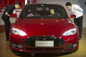 FILE - In this Monday, April 25, 2016, file photo, staff members talk with visitors as they sit inside a Tesla Model S electric car on display at the Beijing International Automotive Exhibition in Beijing.