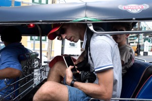 Two male passengers and a driver sit in a tuk-tuk in Bangkok, Thailand.