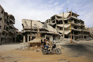 In this May 18, 2017 photo, Syrian ride a motorcycle past destroyed buildings at the mountain resort town of Zabadani in the Damascus countryside, Syria.