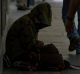 Pedestrians walk past a homeless man sheltering from the rain.