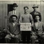 Five men, four with hats, one in middle holding copy of Industrial Worker