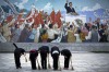 North Korean school girls holding brooms bow to pay their respects toward a mural which shows the late North Korean ...