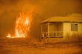 Flames rise behind a vacant house as a firefighter works to halt the Detwiler wildfire near Mariposa, Calif., on ...