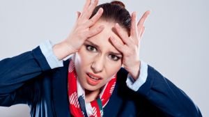 Portrait of young woman with hands on her head looking at the camera. Studio shot, grey background.