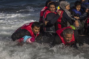 A group of Afghan migrants, including a small child carried through the water by man at left, disembark safely from their frail boat in bad weather on the Greek island of Lesbos after crossing the Aegean see from Turkey, Wednesday, Oct. 28, 2015.