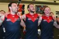 Cameron Pedersen, Jack Watts and Clayton Oliver of the Demons sing the song in the rooms after a wonderful win. 