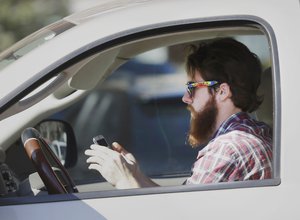 A man works his phone as he drives through traffic in Dallas, Tuesday, Feb. 26, 2013. Texas lawmakers are considering a statewide ban on texting while driving.