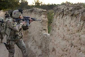 File - A U.S. soldier provides security and scans the area through a mud wall as Czech and Afghan soldiers conduct a mission through a village in Parwan province, Afghanistan, Oct. 20, 2015.