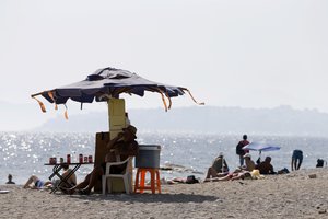 A vendor sits under an umbrella on the beach at the Athens' southern suburb of Paleo Faliro, Tuesday, July 25, 2017.