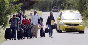 Migrants wheel their luggage down Roxham Road in Champlain, N.Y., while heading to an unofficial border station across from Saint-Bernard-de-Lacolle, Quebec, Monday, Aug. 7, 2017.