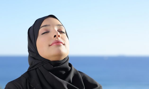 A Saudi Arabian woman in hijab breathes deeply at a local beach. Photo: iStock/Getty Images