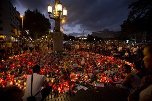 People stand next to candles and flowers placed on the ground, after a terror attack that killed at least 14 people and wounded over 120 in Barcelona, Spain, Sunday, Aug. 20, 2017.