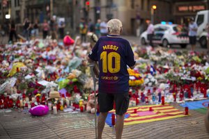 A man stands next to flags, flowers, messages and candles to the victims on Barcelona's historic Las Ramblas promenade on the Joan Miro mosaic, embedded in the pavement where the van stopped after killing at least 14 people in Barcelona, Spain, Monday, Aug. 21, 2017.