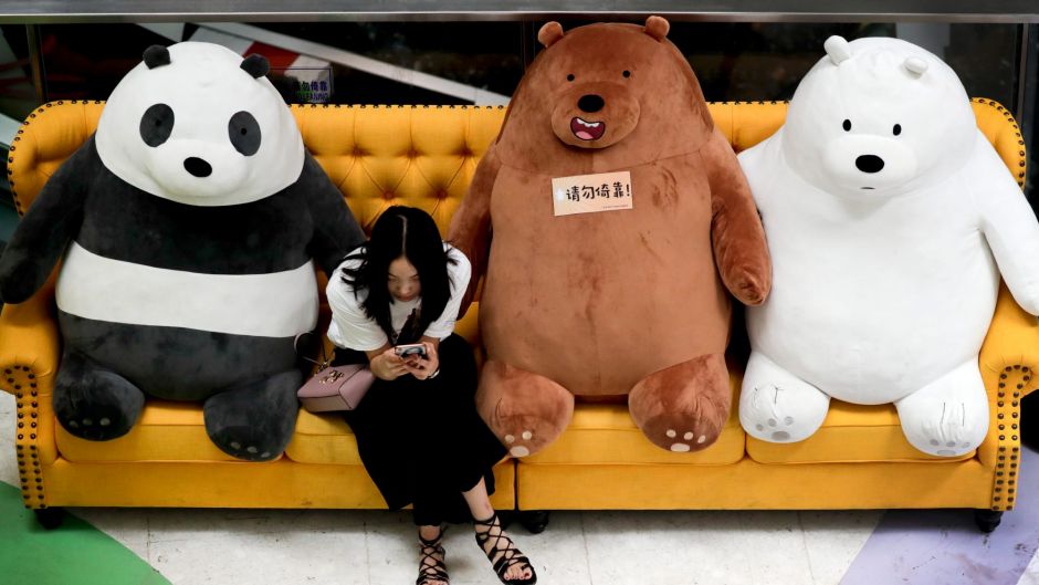 A Chinese woman browses a smartphone on a sofa displaying a panda and bears at a shopping mall in Beijing, Monday, Aug. ...