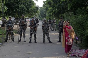 A supporter of the Dera Sacha Sauda religious sect squat others to join her as Indian paramilitary soldiers stand guard on a barricaded road leading to a court in Panchkula, India, Friday, Aug. 25, 2017.