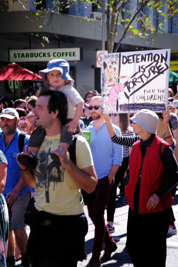 Placard against children in detention; child on man's shoulders 