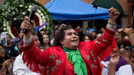 A Juan Gabriel imitator performs by a statue of the superstar, top left, where his fans gather on the one year ...