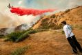 Aaron Funk waters down the hillside behind his parents' home as a plane makes a drop in Sun Valley neighborhood, north ...