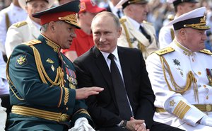 Russian President Vladimir Putin, center, smiles chatting with Defence Minister Sergei Shoigu during military parade during the Navy Day celebration in St.Petersburg, Russia