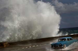 A driver maneuvers his classic American car along a wet road as a wave crashes against the Malecon in Havana, Cuba, Oct. 25, 2012