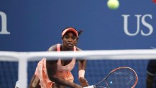 Sloane Stephens follows through after a serve. The ball is seen above the net in the foreground.