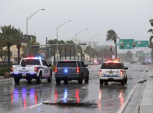 Police cars block a road strewn with debris from roof damage caused by high winds brought on by Hurricane Irma, Saturday, Sept. 9, 2017, in Sunny Isles Beach, Fla.