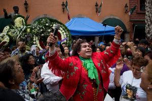 A Juan Gabriel imitator performs by a statue of the superstar, top left, where his fans gather on the one year ...