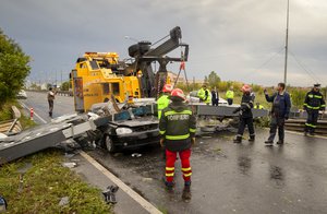 Emergency workers stand around a car that was destroyed by a traffic sign that fell due to heavy winds killing the driver in Timisoara, Romania, Sunday, Sept. 17, 2017, following a deadly storm that affects the west part of the country.