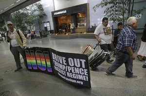 Protester Xochitl Johnson, left, holds up a sign as travelers walk past at San Francisco International Airport in San Francisco, Thursday, June 29, 2017.