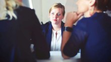 Three women in business clothing sit at a table.