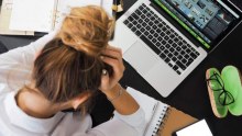 A young woman sits with her head in her hands at her desk.