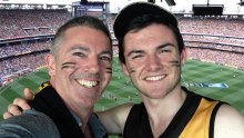 Guy Stayner with his son Zack in the stands with a crowded MCG in the background.