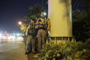 Police officers take cover near the scene of a shooting near the Mandalay Bay resort and casino on the Las Vegas Strip, Sunday, Oct. 1, 2017, in Las Vegas.