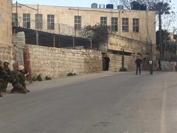 An Israeli soldier aims his rifle at Palestinians making their way past the boys’ school