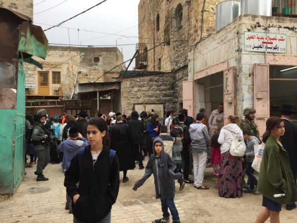 A group of colonial settlers make their way through the Palestinian souk, escorted by heavily armed Israeli forces.