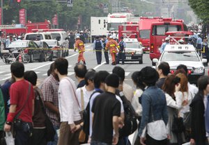 In this June 8, 2008 file photo, pedestrians look at rescuers and police investigators working at the crime scene in Tokyo's Akihabara district after a Japanese man rammed a truck into a crowd of shoppers, jumped out and went on a stabbing spree, killing seven people and wounding 10 others, in  case of a worker whose death was ruled by a Japanese court as caused by overwork