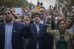 Catalan President Carles Puigdemont, centre, deputy president Oriol Junqueras, left, and Carme Forcadell, speaker of the house in the Catalan parliament, hold hands during a protest against the National Court's decision to imprison civil society leaders, in Barcelona, Spain, Saturday, Oct. 21, 2017.