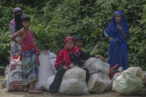 A Rohingya Muslim family, which crossed over from Myanmar into Bangladesh, sits on a roadside along with their belongings after the government moved them to newly allocated refugee camp areas, near Kutupalong, Bangladesh, Sunday, Oct. 22, 2017.