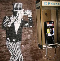 Uncle sam, rendered in graffiti on brick wall, next to a payphone wiretapping your calls