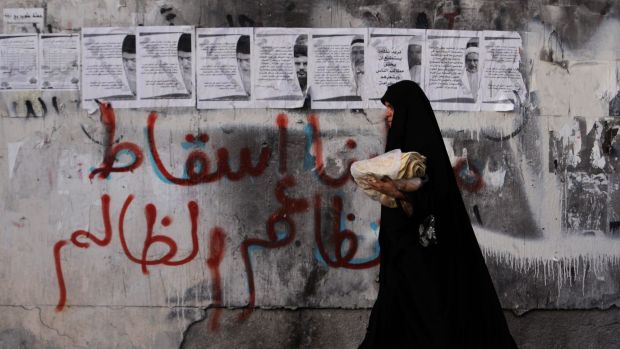 A women carries bread past a wall in the village of Karzakan, Bahrain, with graffiti reading "our demand is the fall of ...