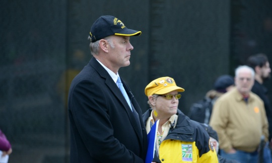 Secretary Zinke wearing a coat and a ballcap stands by a volunteer at the black wall of the Vietnam Veterans Memorial.