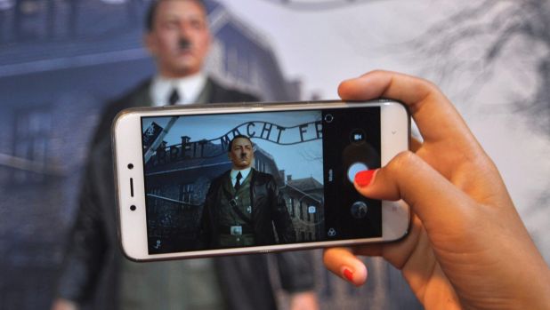 A visitor takes a photo of Adolf Hitler displayed against the backdrop of an image of Nazi Death Camp Auschwitz-Birkenau ...