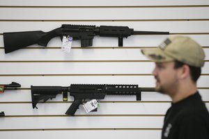 In this Dec. 9, 2015, photo, a sales associate walks past semiautomatic rifles at Bullseye Sport gun shop in Riverside, Calif.