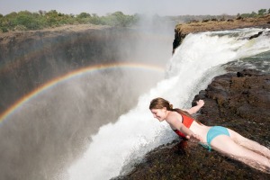 A woman in Devil's Pool hangs over the edge of Victoria Falls.