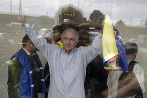 Holding a national Venezuelan flag, ousted Caracas Mayor Antonio Ledezma waves from inside El Dorado international airport