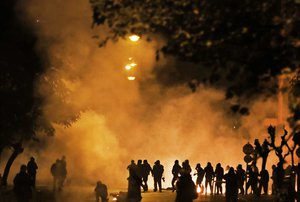 Tear gas fired by police billows in the sky as protesters gather around burning barricades during clashes in Athens, Friday, Nov. 17, 2017.