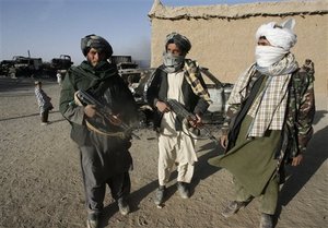 In this photo taken Monday, Oct.19, 2009, Taliban militants stand beside the burnt trucks, background left, on main Ghazni- Kandahar highway in Ghazni, west of Kabul, Afghanistan. Taliban militants set fire to 15 trucks carrying supplies to a military base in eastern Ghazni province, according to local official Sahib Khan. Afghan security guards killed two militants during the fighting.